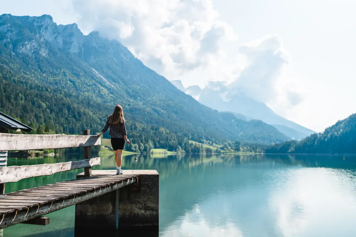See mit Steg und Person vor Bergkulisse